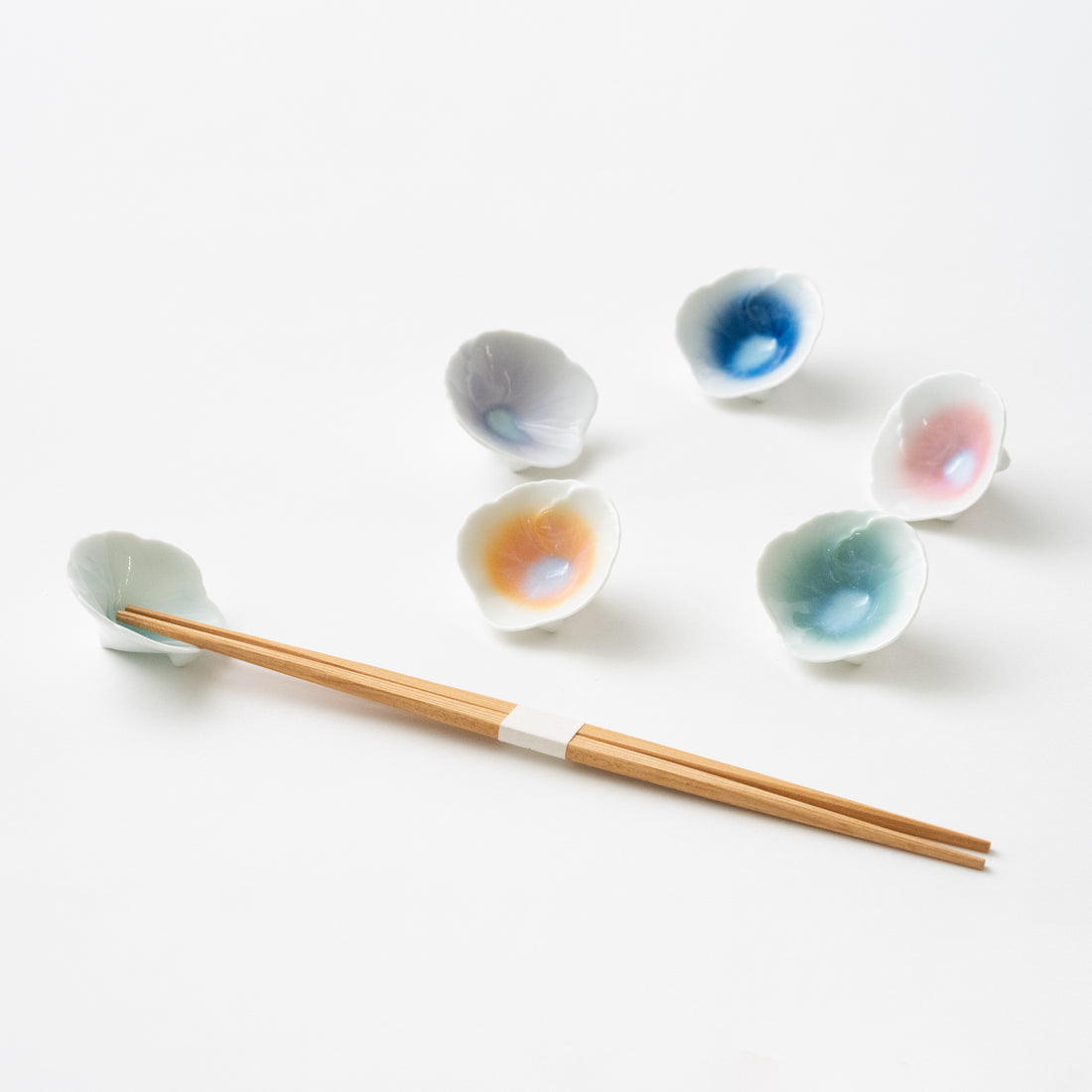 Ceramic chopstick rests in the shape of a flower. Colors in blue, orange, green, pink and lavender. Comes in a wooden box